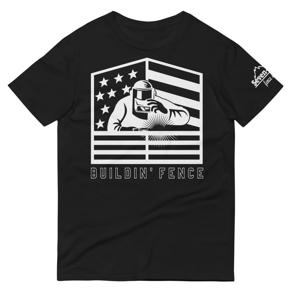 A Welder welding fence with his hand on his welding mask and an american flag behind him with the text Buildin' Fence