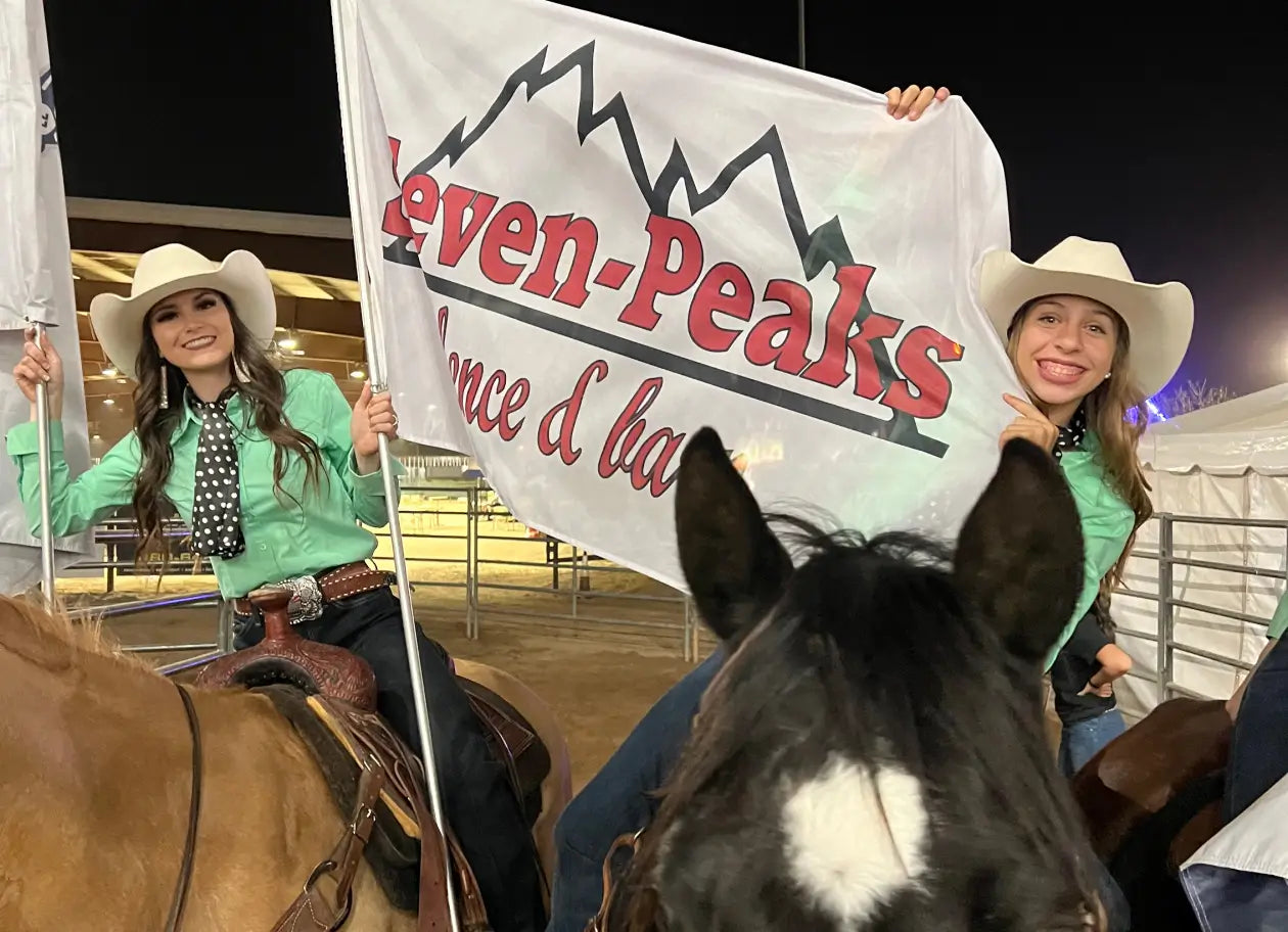 "rodeo cowgirls holding Seven Peaks flag on horses"