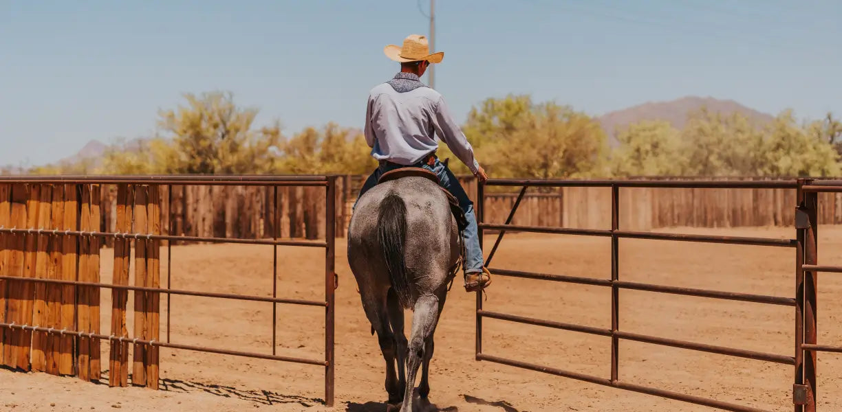 cowboy riding horse through gate in desert ranch setting