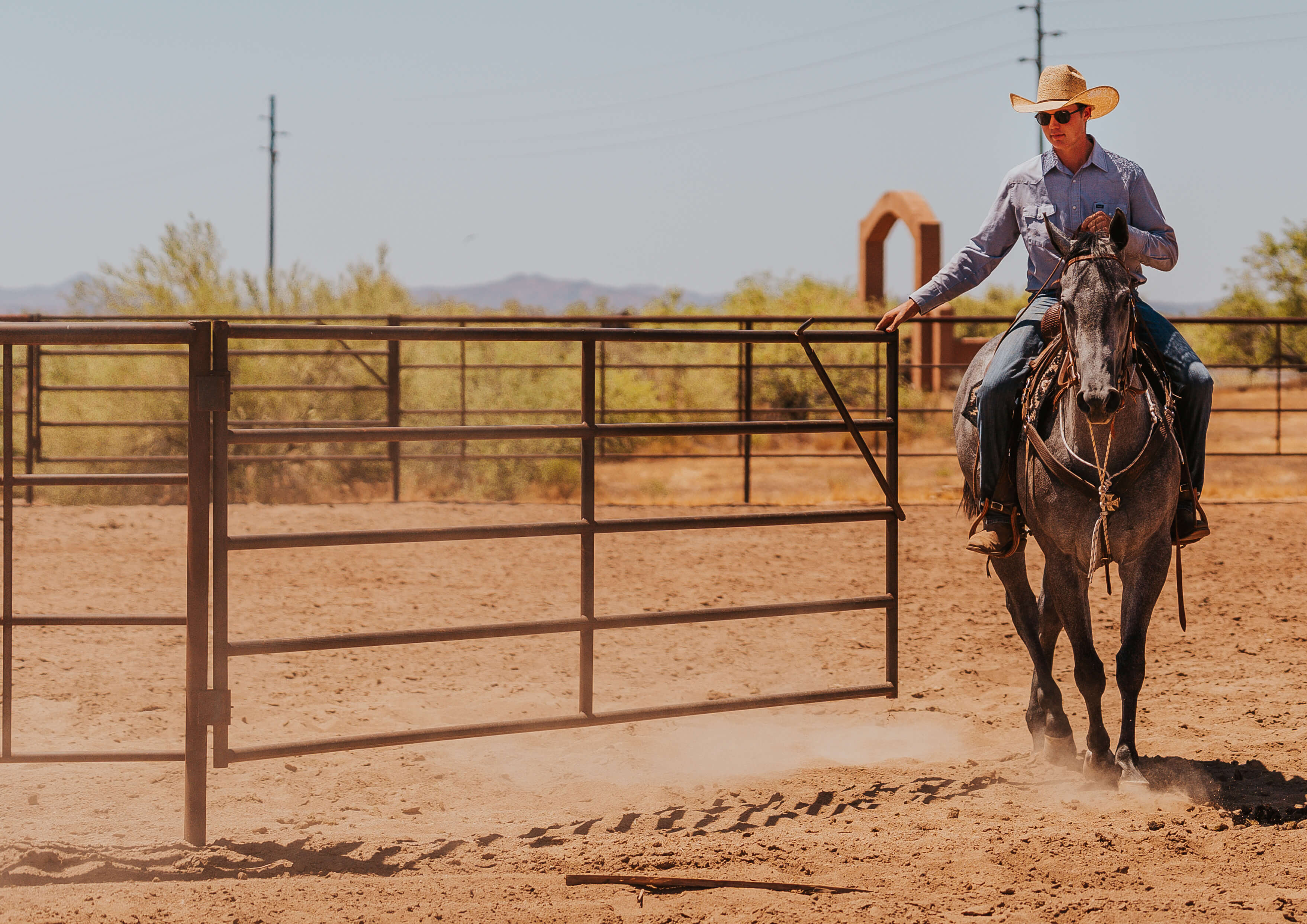 Cowboy riding horse near gate in desert ranch setting