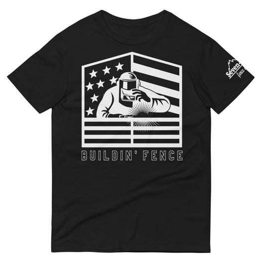 A Welder welding fence with his hand on his welding mask and an american flag behind him with the text Buildin' Fence